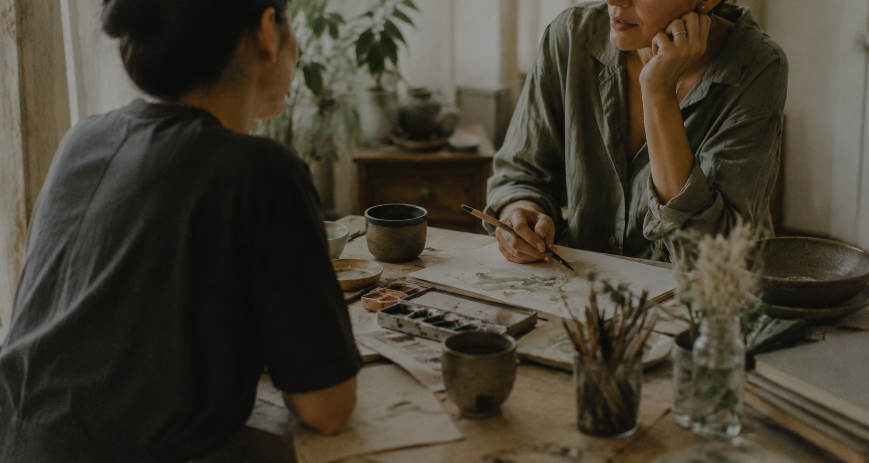 Two people at a table with watercolor and brushes, mid conversation