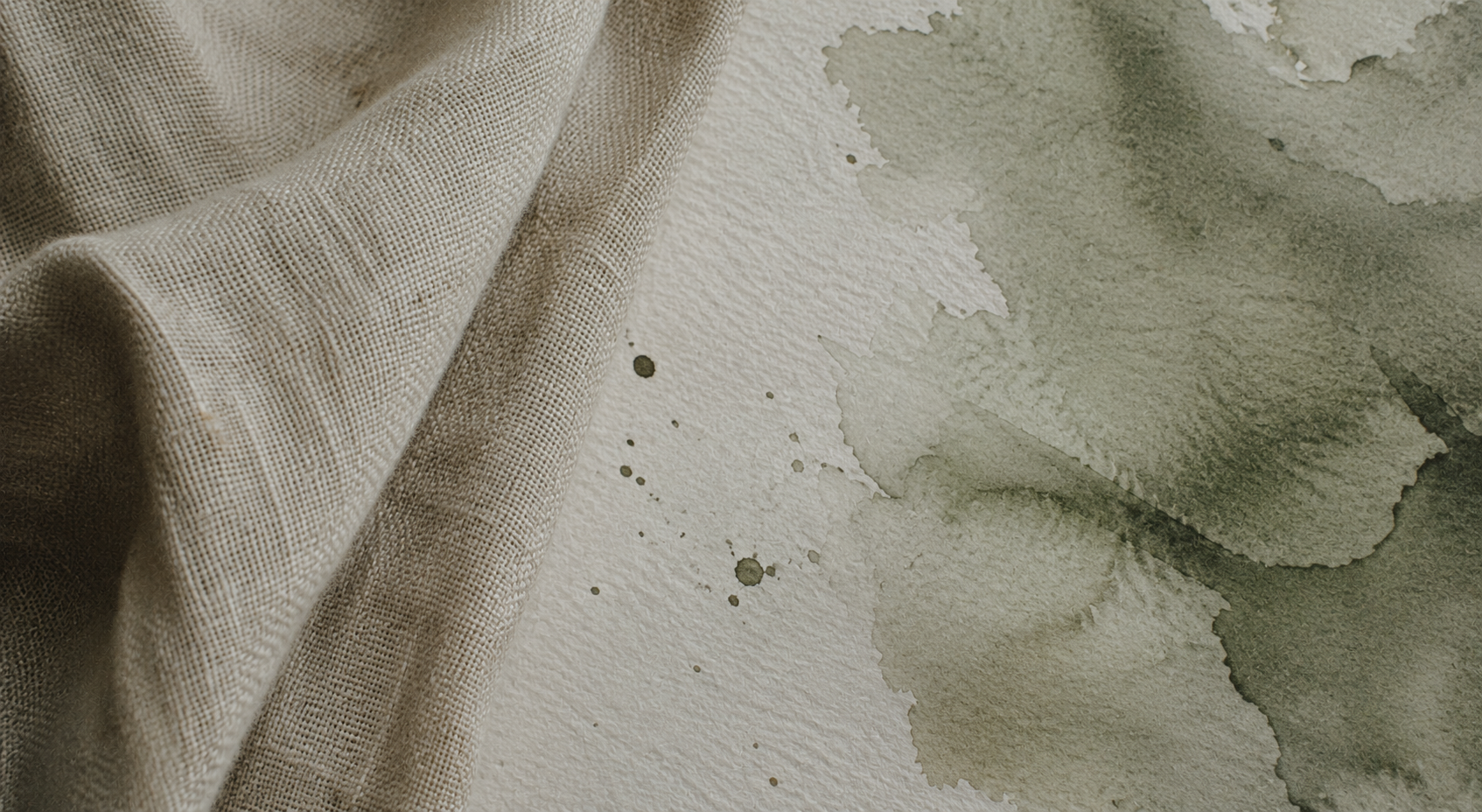 Linen fabric beside watercolor paper with sage green wash