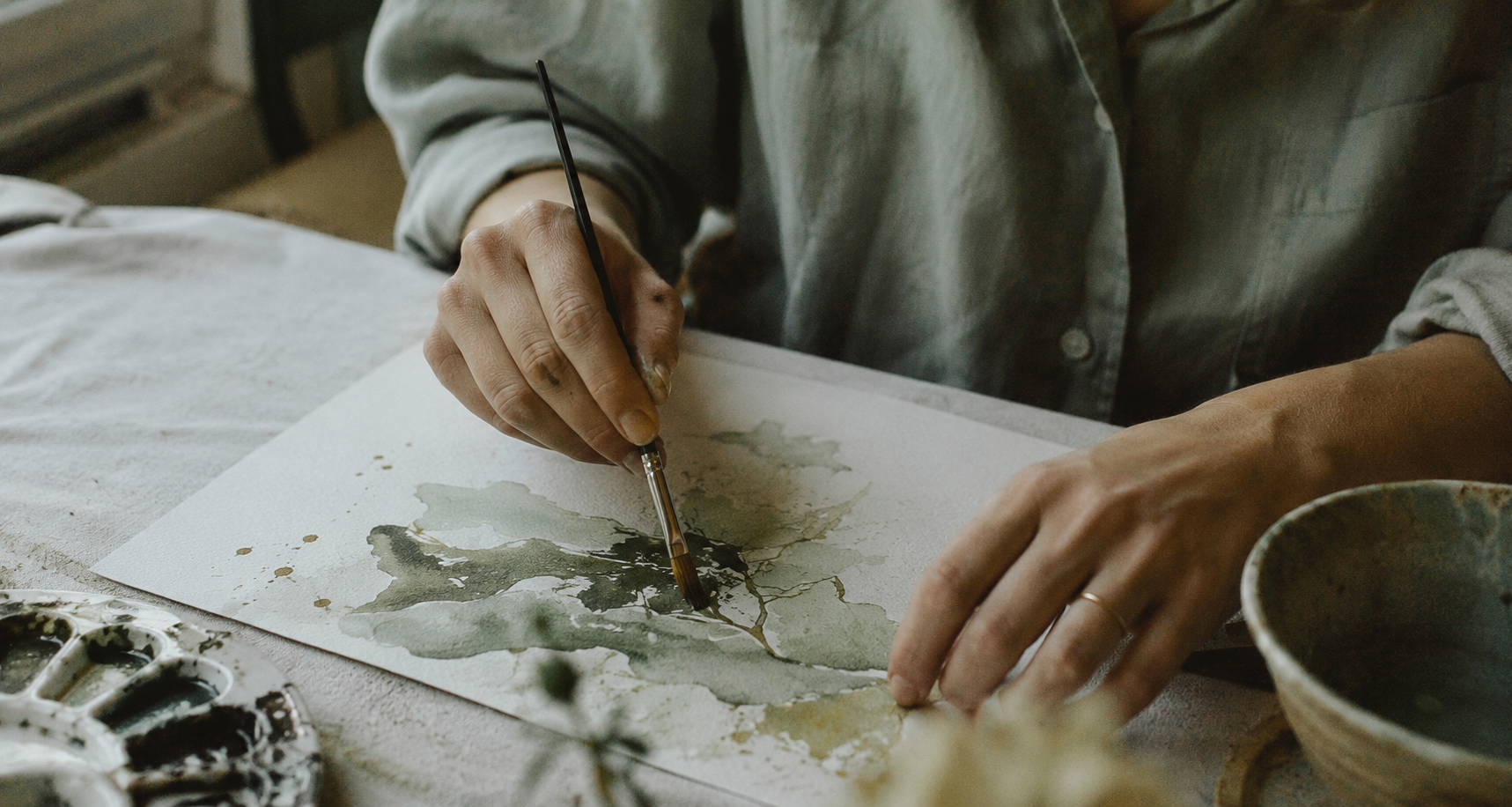Hands painting with watercolor on textured paper, natural light